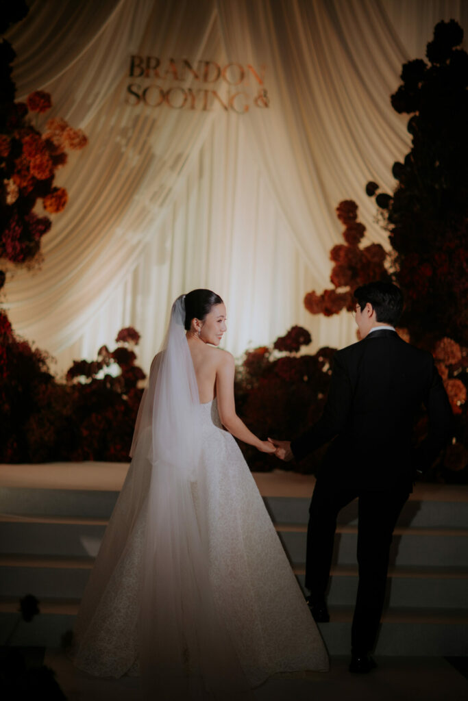 Bride and groom ascend steps, floral decor, Brandon & Soo Ying above.