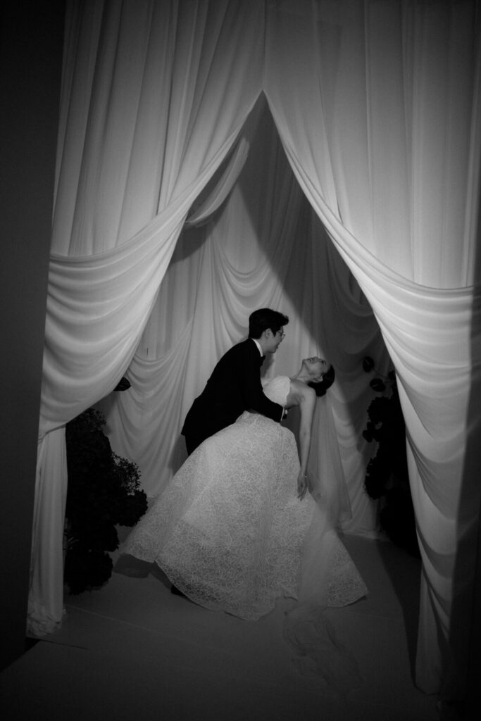 Bride in Mira Zwillinger gown kisses groom under curtains.