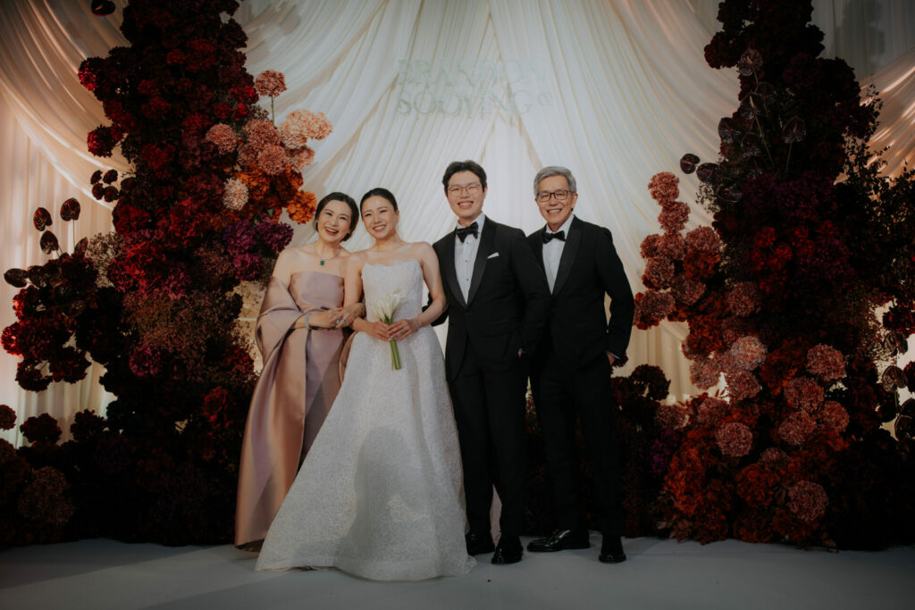 Bride Katya Ruiz with loved ones before flower backdrop.