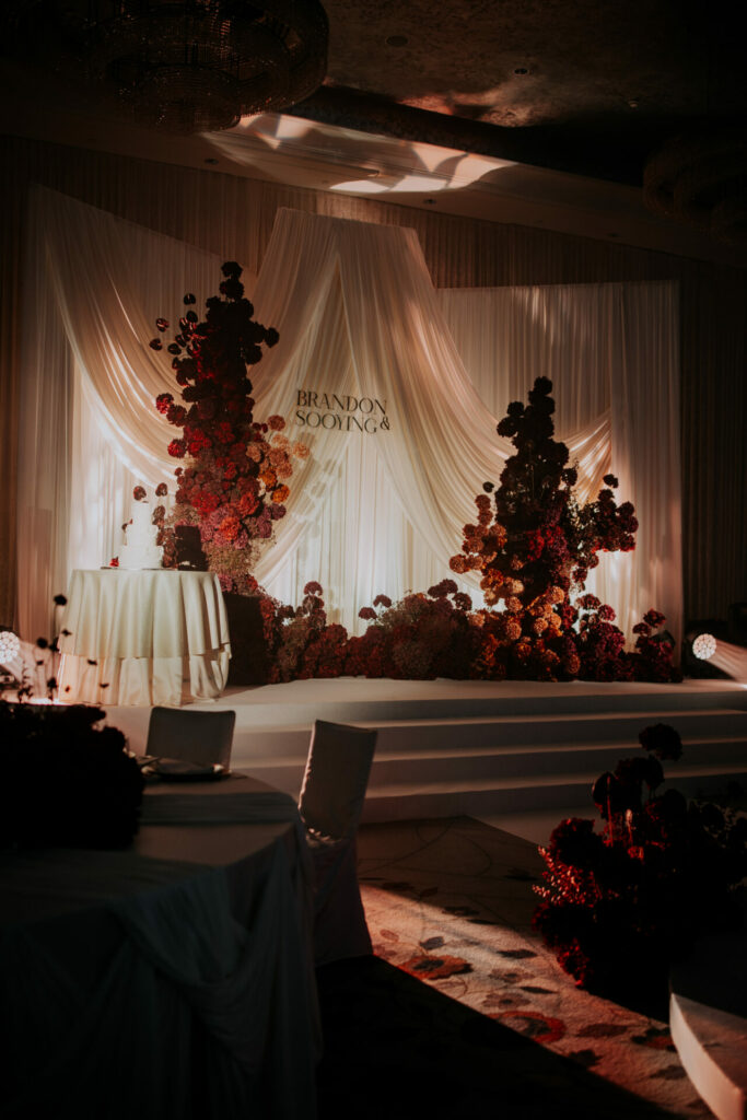 Katya Ruiz on elegant wedding stage, red florals, draped fabric.