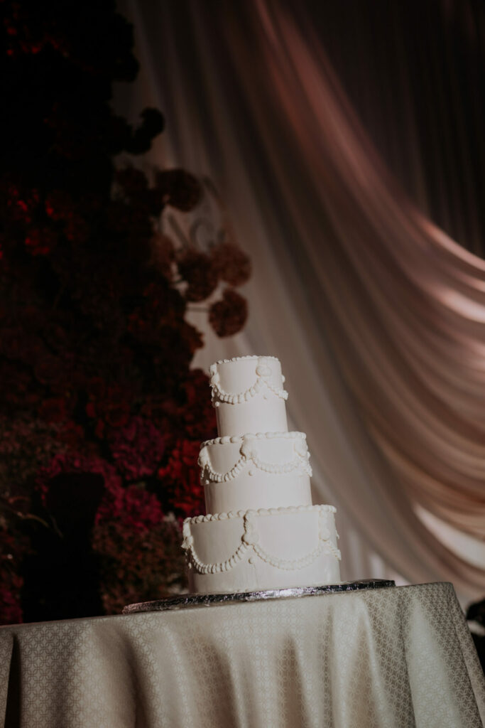 Elegant four-tier white cake with pearls, luxury backdrop.