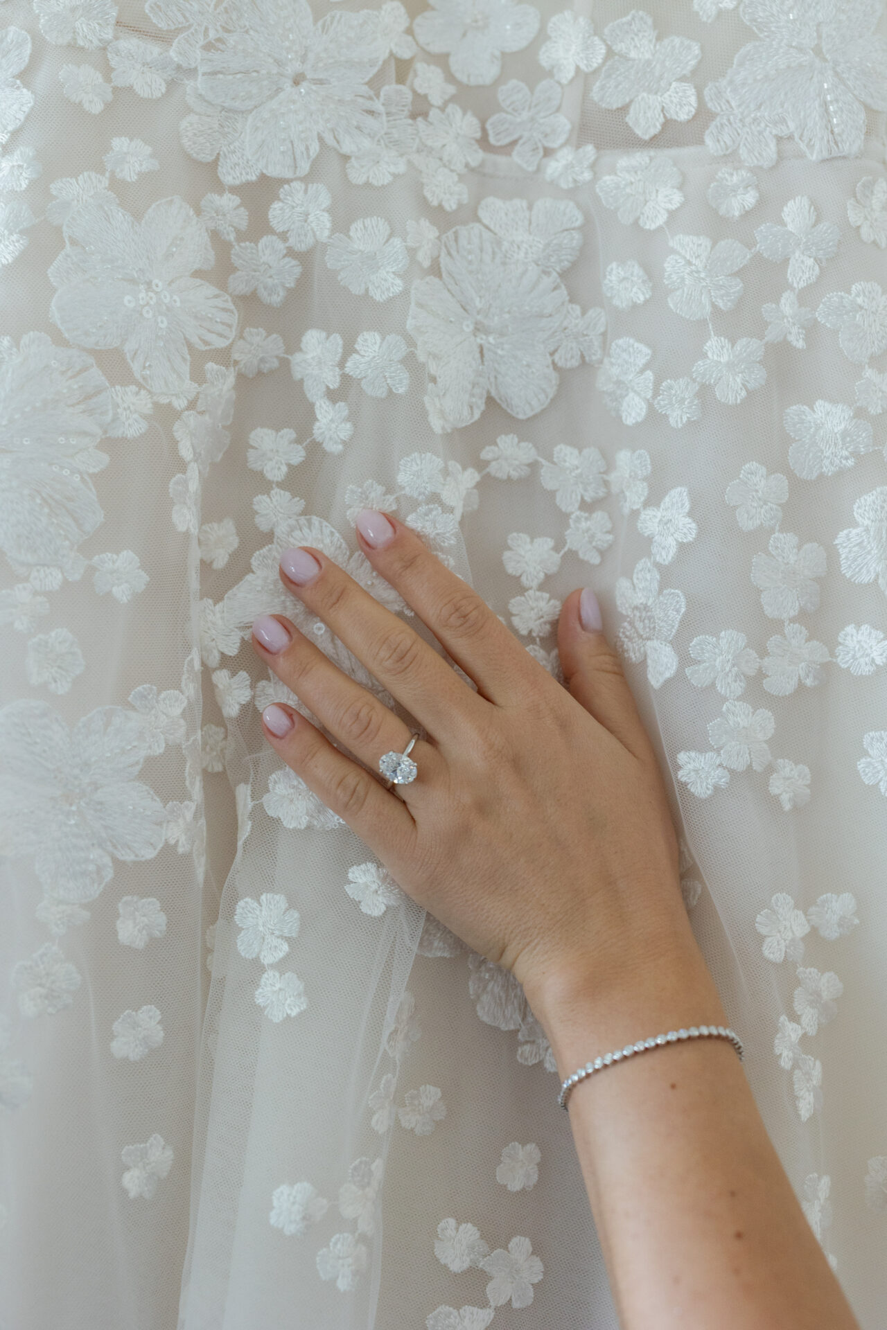 Pink-nailed hand with ring on floral lace fabric.