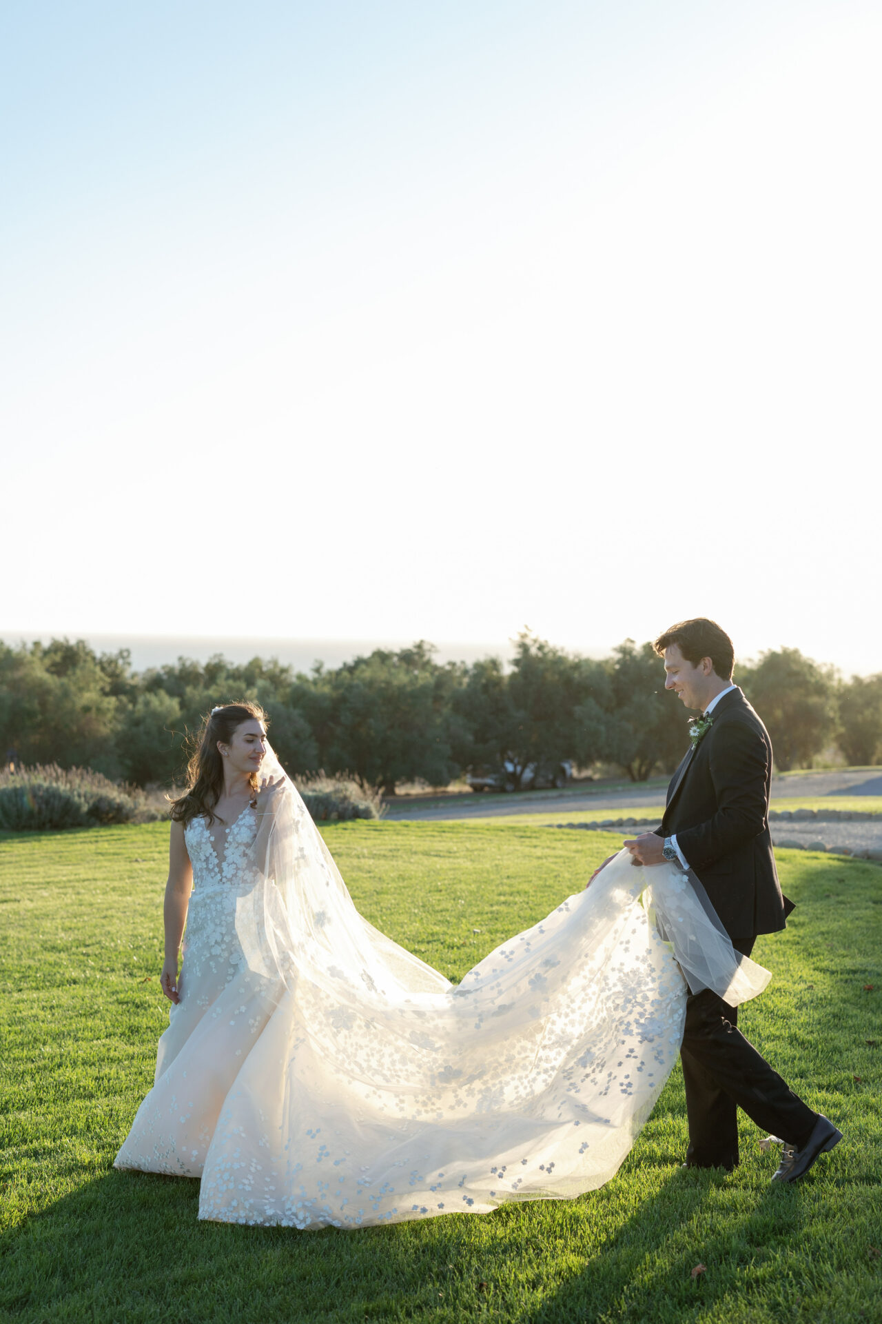Bride and groom on lawn; groom lifts bride’s train.