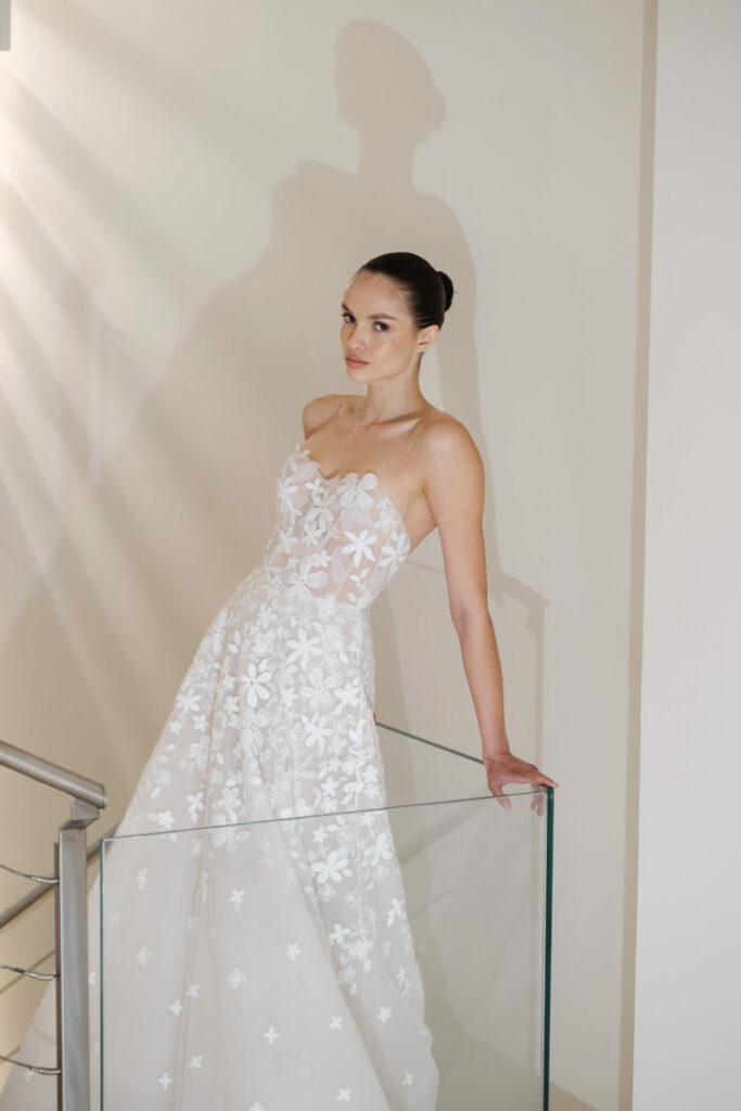 Woman in white lace gown leans on railing.