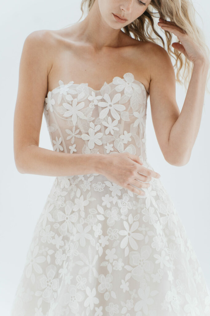 Woman in sheer strapless wedding dress touches hair.