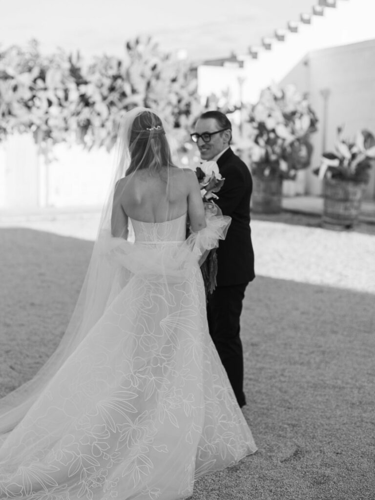 Bride with bouquet faces suited man; black and white.