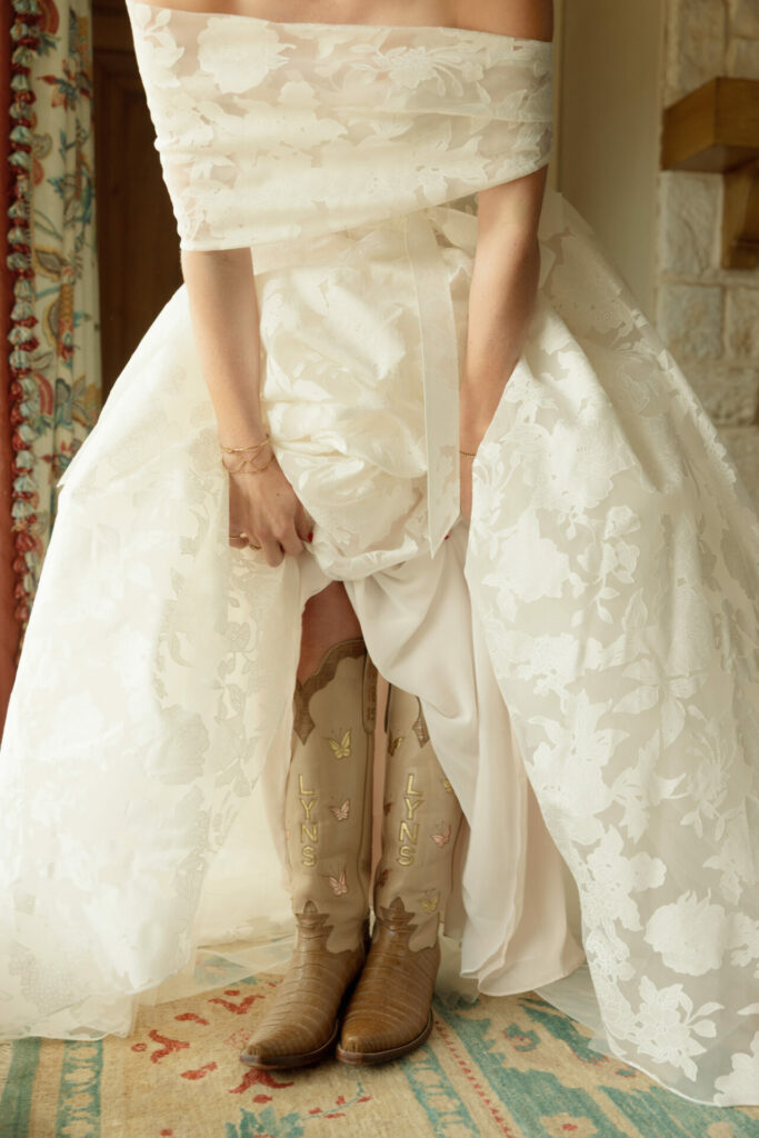 Bride lifts floral gown indoors, revealing butterfly cowboy boots.