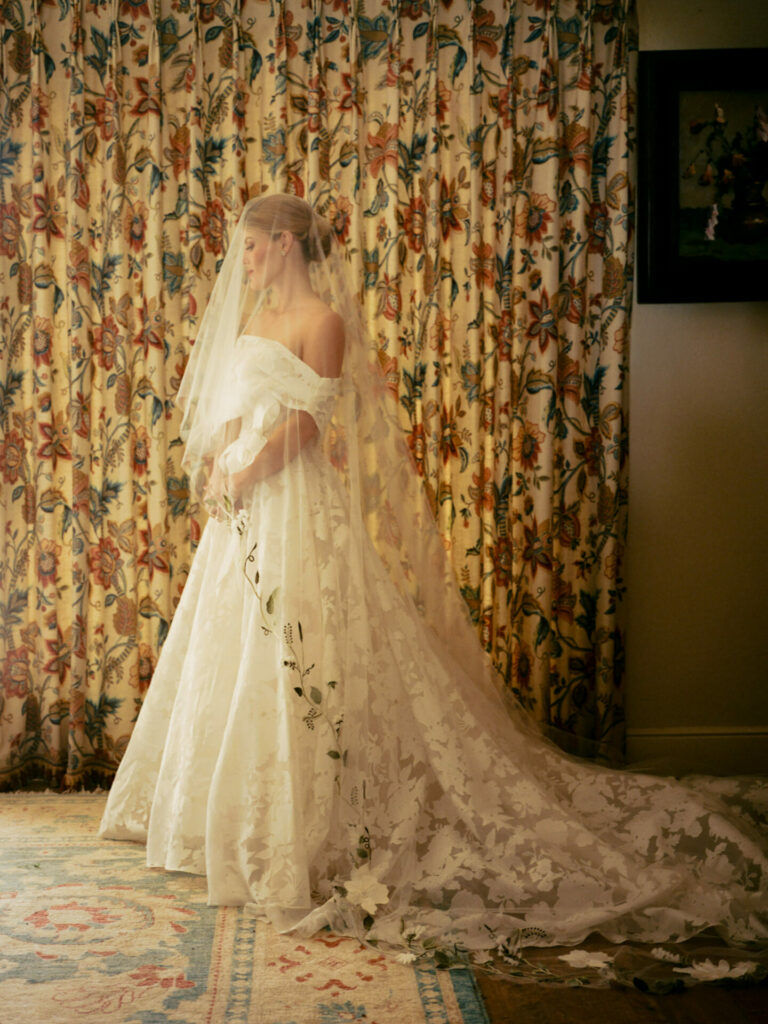 Bride Katya Ruiz in floral Mira Zwillinger gown by window.