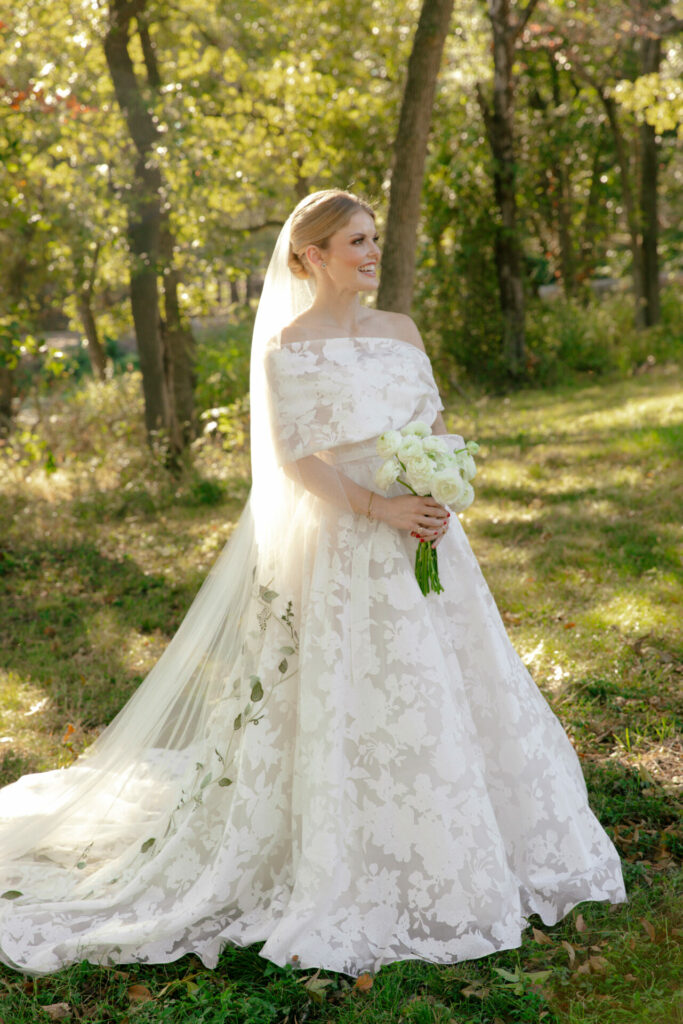 Katya Ruiz in sunlight, white roses, couture gown, veil flowing outdoors.