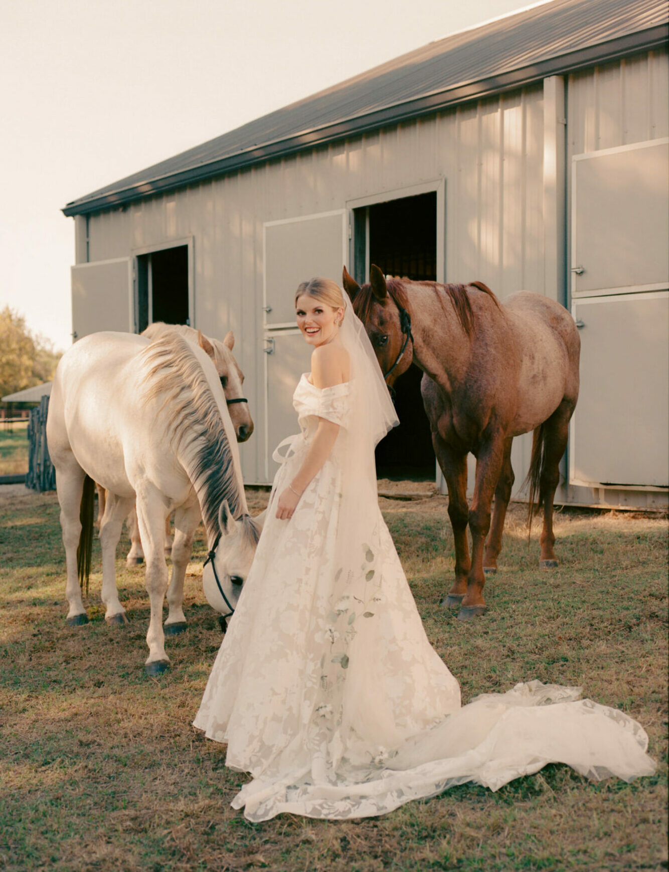 Katya Ruiz in couture gown by horses near barn.