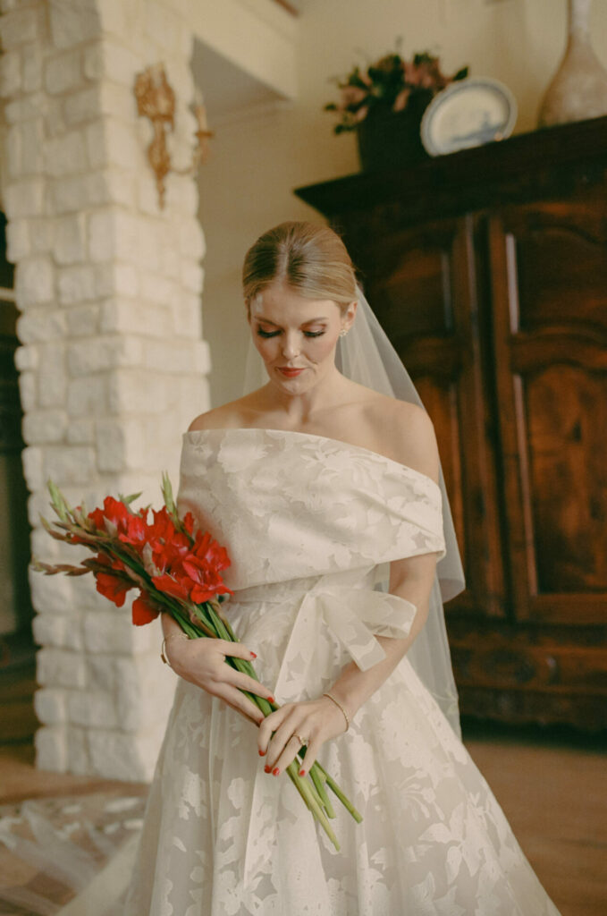 Bride in luxurious Amy gown, red bouquet, calm indoors.