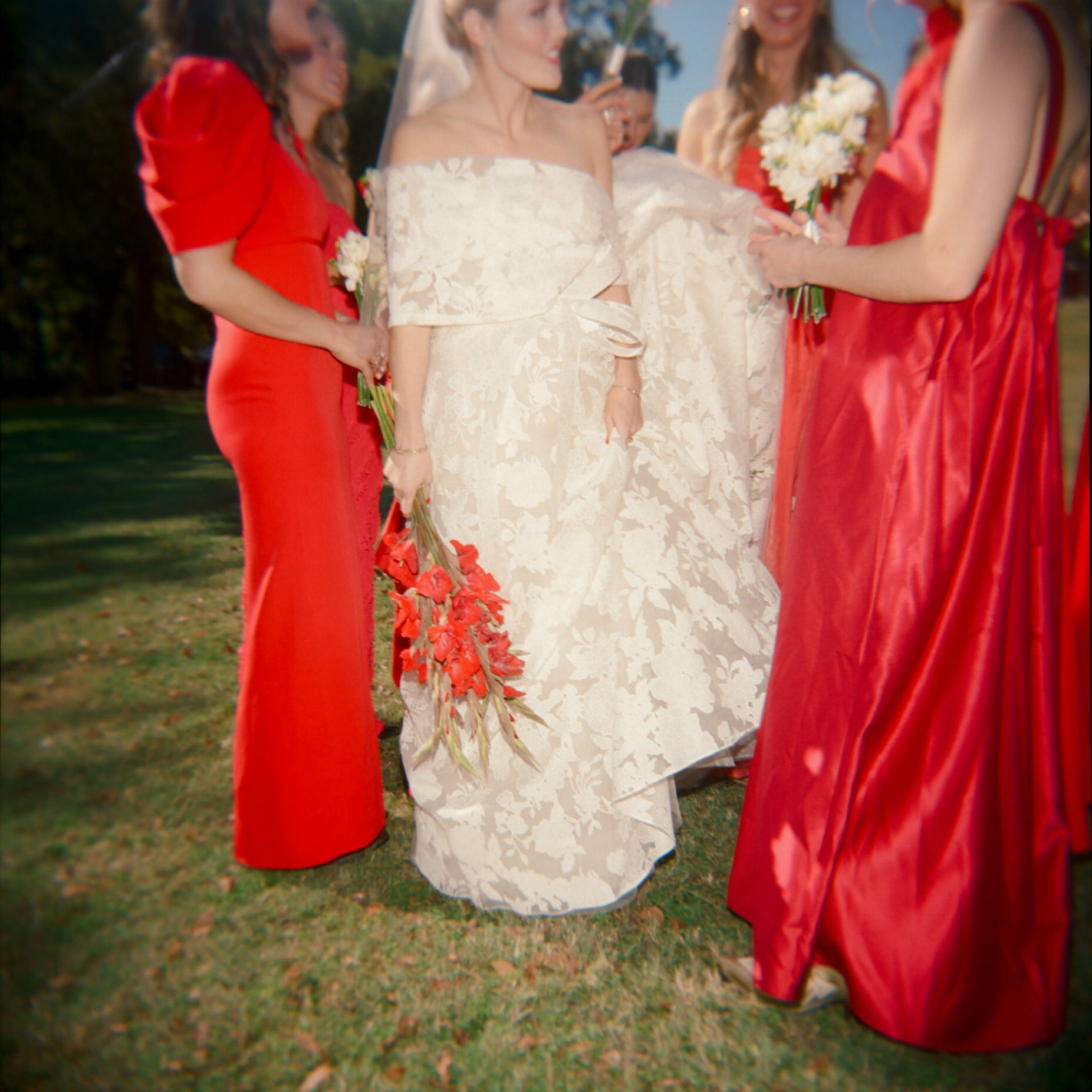 Bride in luxury gown, red bouquet, bridesmaids in red.