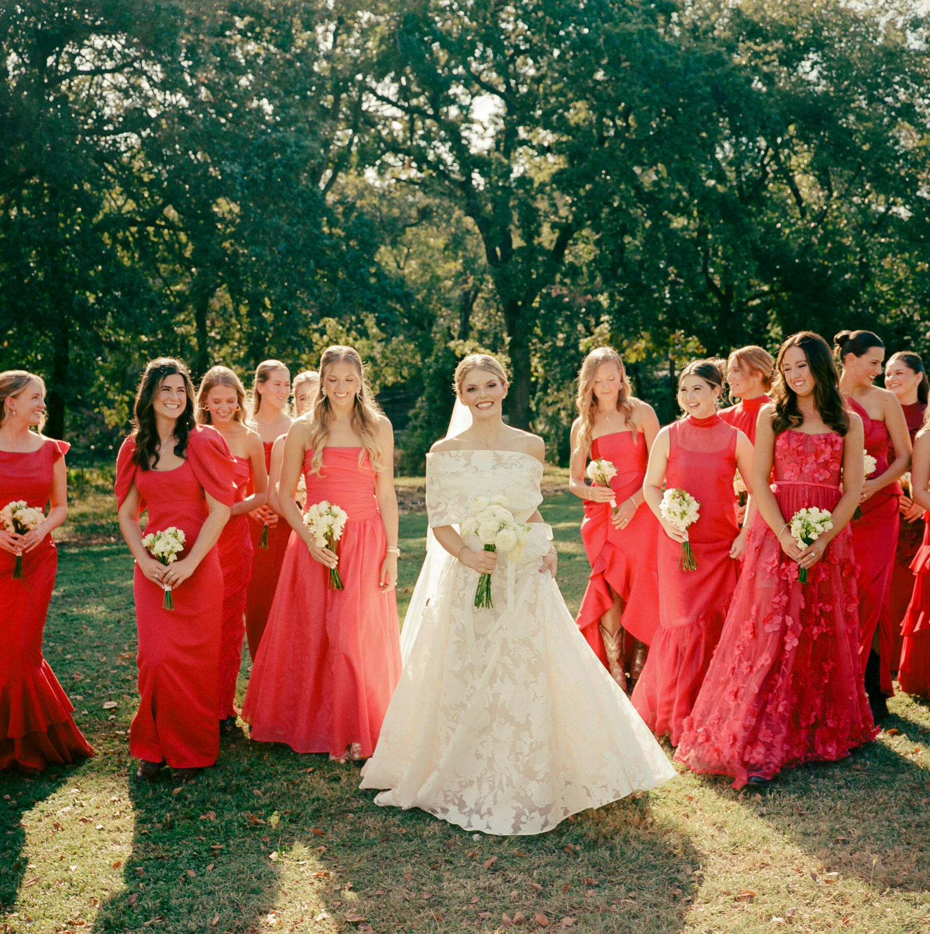 Bride in couture gown with red-dressed bridesmaids outdoors.