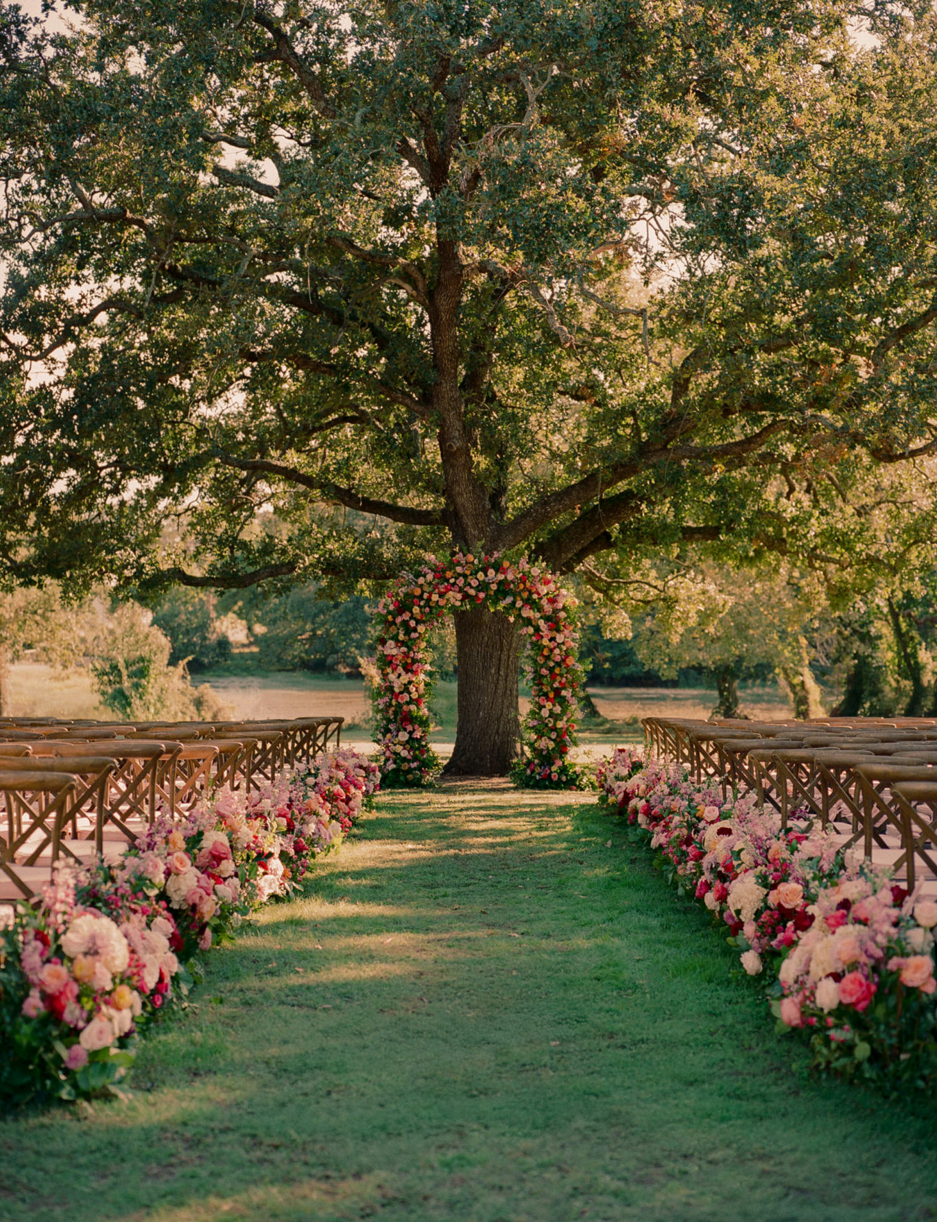 Floral-lined grassy aisle leads to tree and bridal arch.