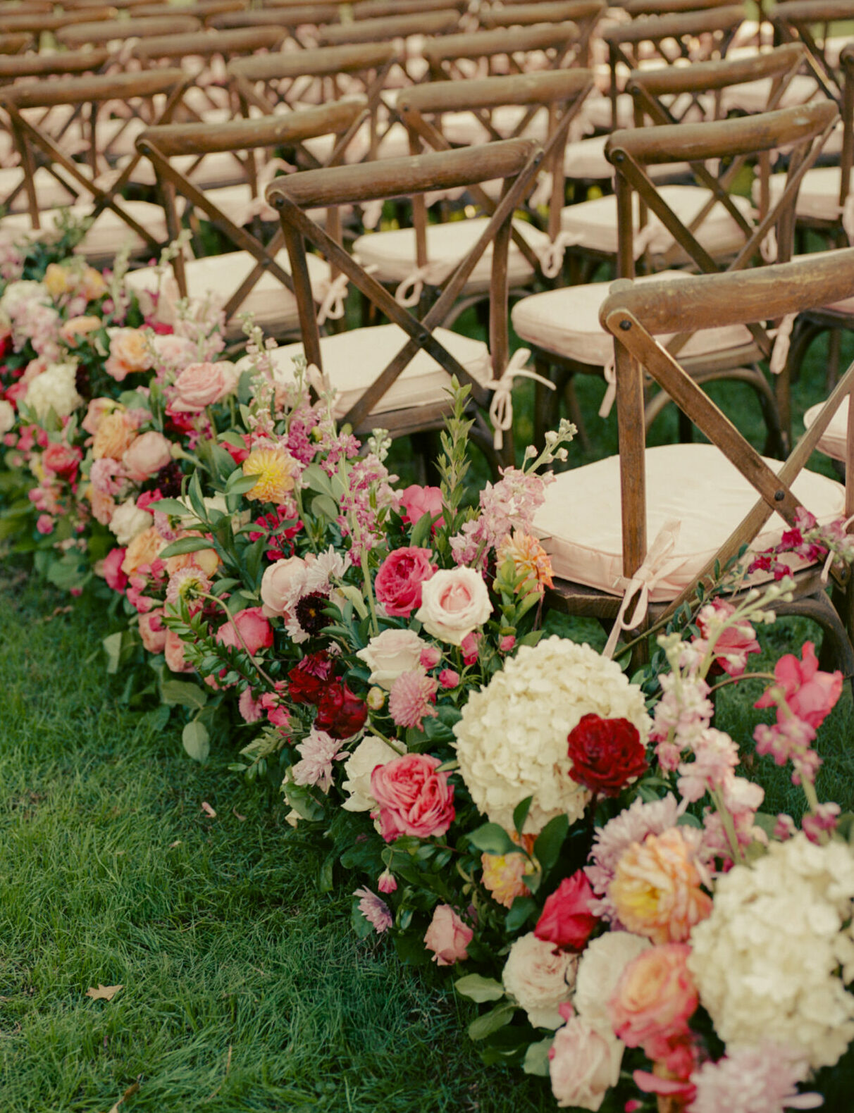 Wooden chairs on grass, colorful blooms, bridal elegance.