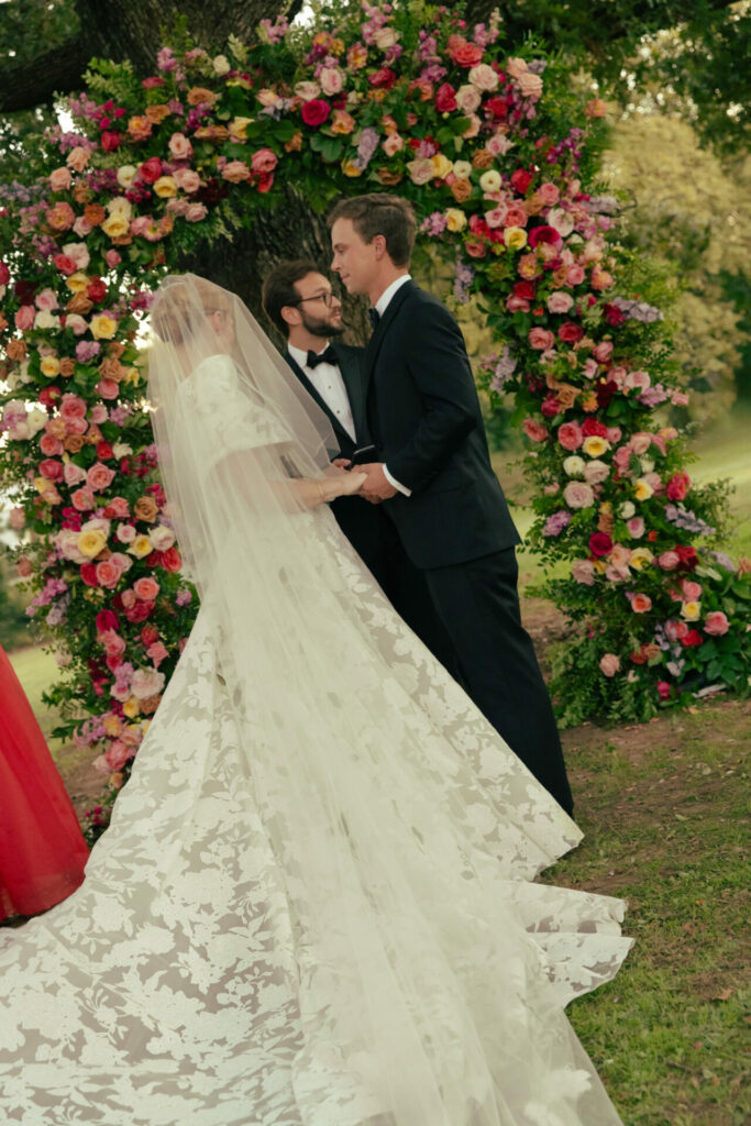 Katya Ruiz weds in Amy gown under vibrant floral arch.