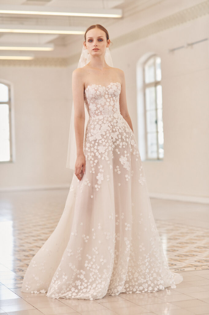 Woman in strapless white floral wedding gown in sunlit room.
