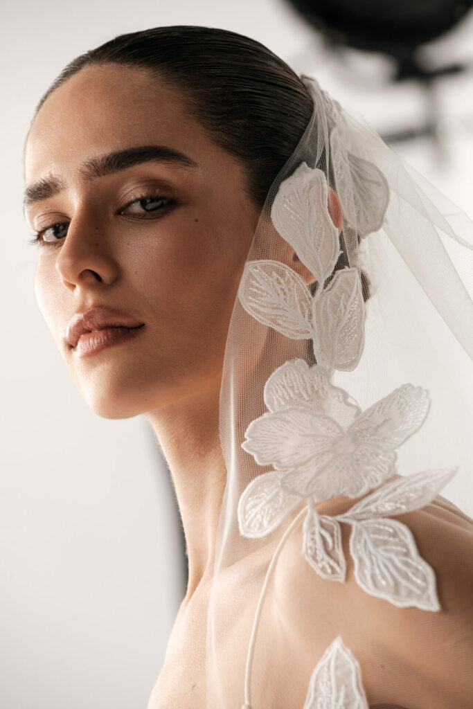 Woman in embroidered veil gazes confidently over shoulder.