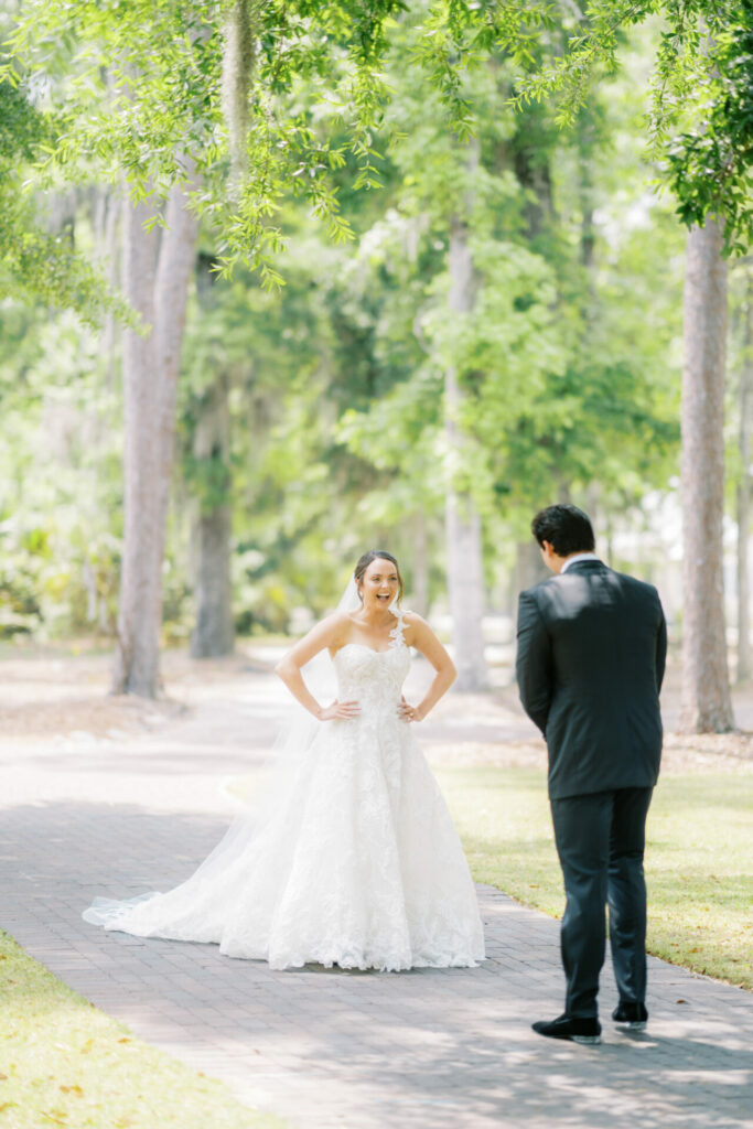 Bride in lace gown smiles at groom outdoors.