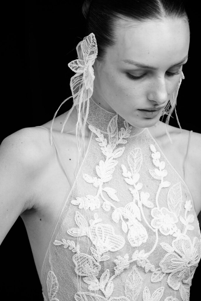 Person in sheer, floral high-neck, lace earrings, monochrome.