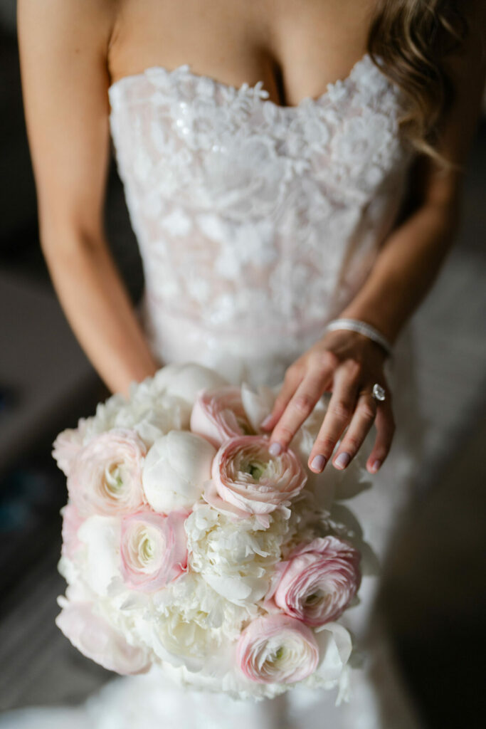Bride in lace gown shows diamond ring, holding roses.