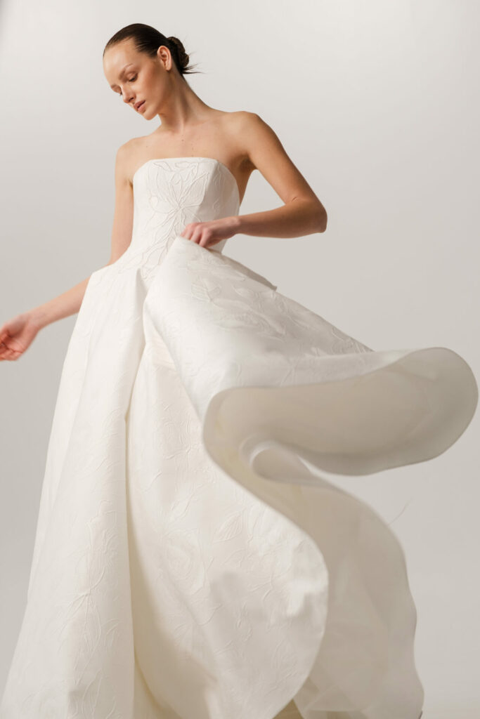 Woman in strapless white gown holding flowing fabric.
