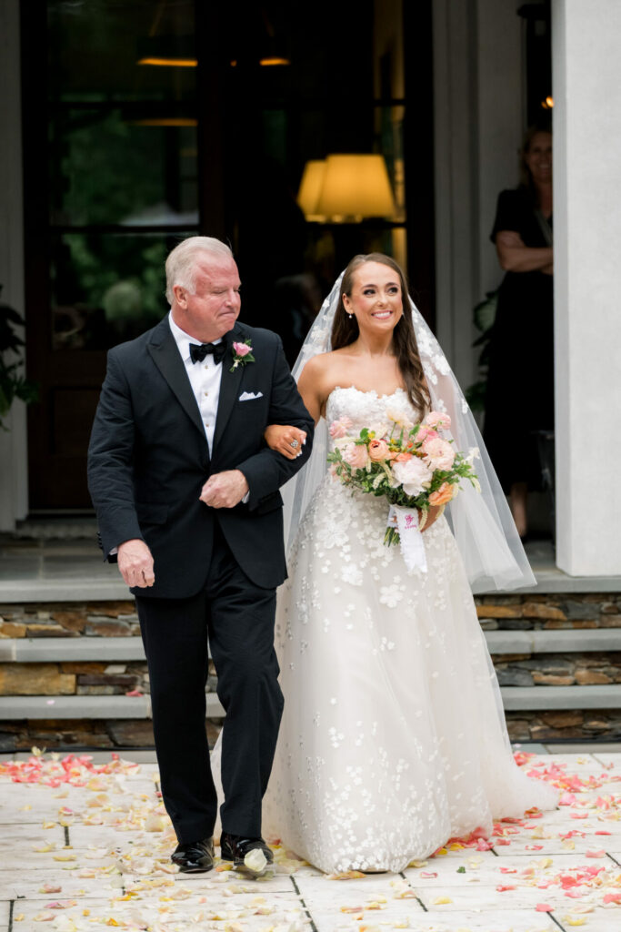 Katya Ruiz in floral gown walks aisle with older man.