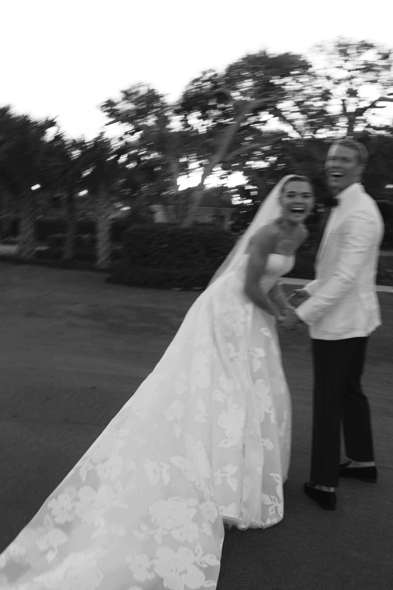 Laughing bride and groom outdoors in blurred black-and-white.