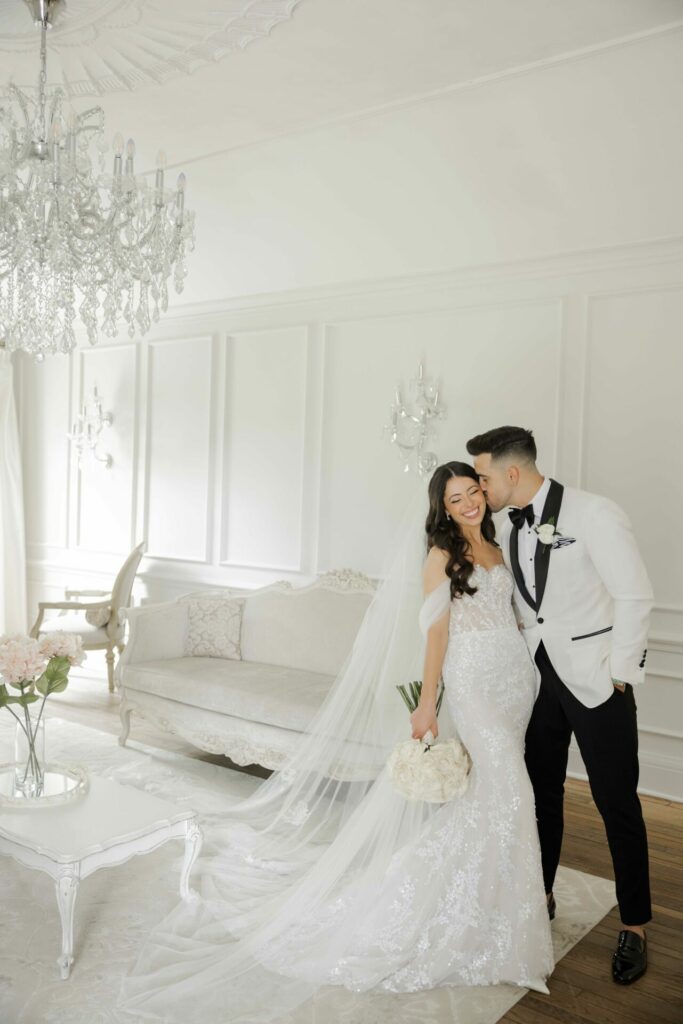 Bride and groom share a forehead kiss in elegant room.