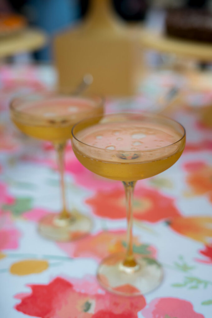 Two coupe glasses with pale orange cocktails on floral cloth.