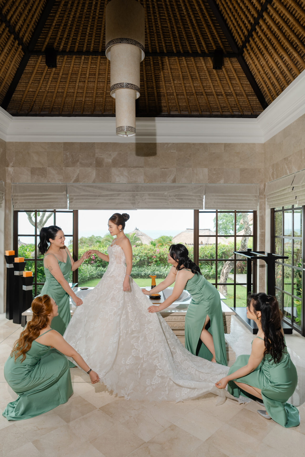 Bride in white gown with bridesmaids, sunny rustic room.