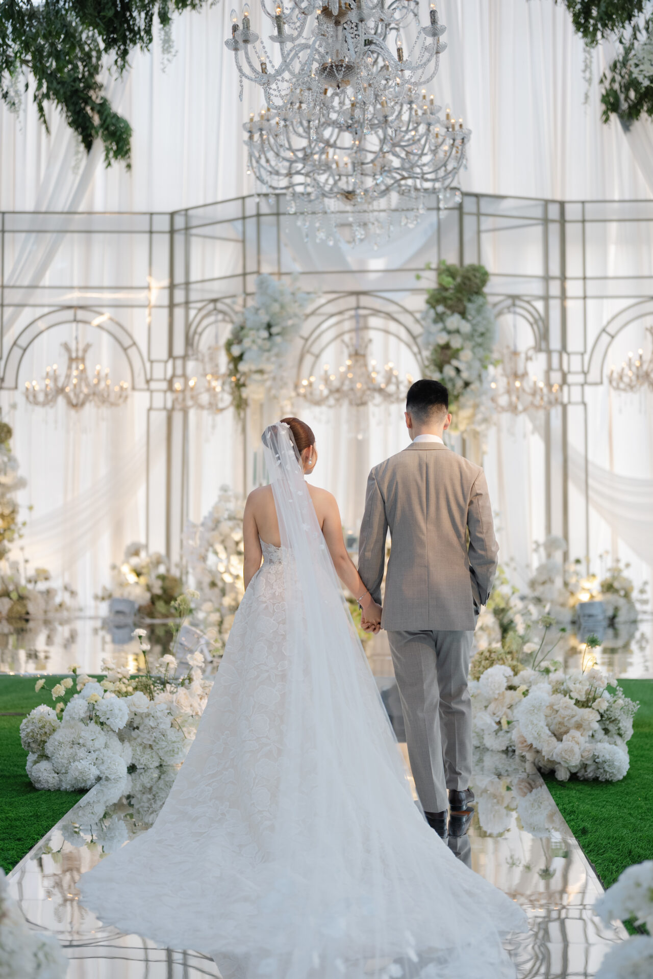 Bride and groom walk down mirrored, flower-lined aisle.