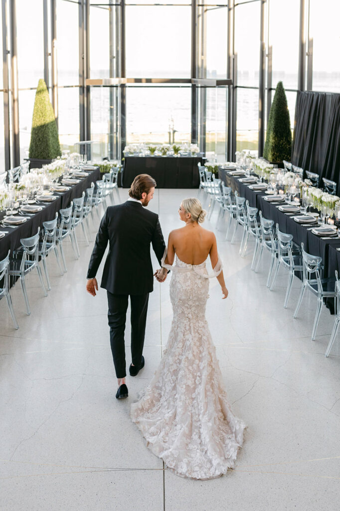 Bride and groom walk in modern glass venue, elegant banquet.