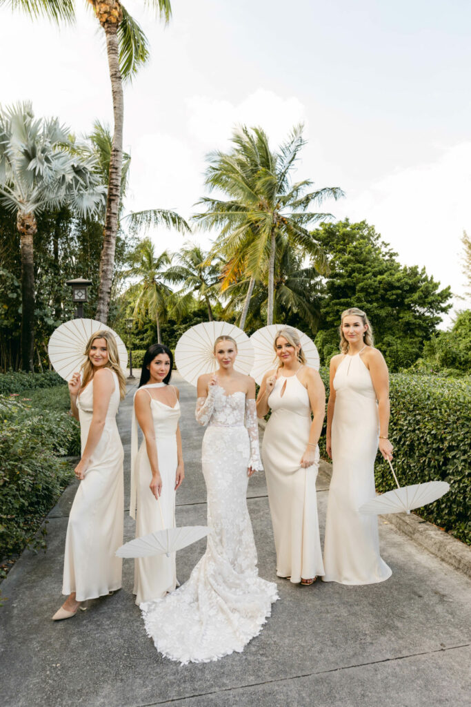 Bride and bridesmaids with parasols amid lush greenery.