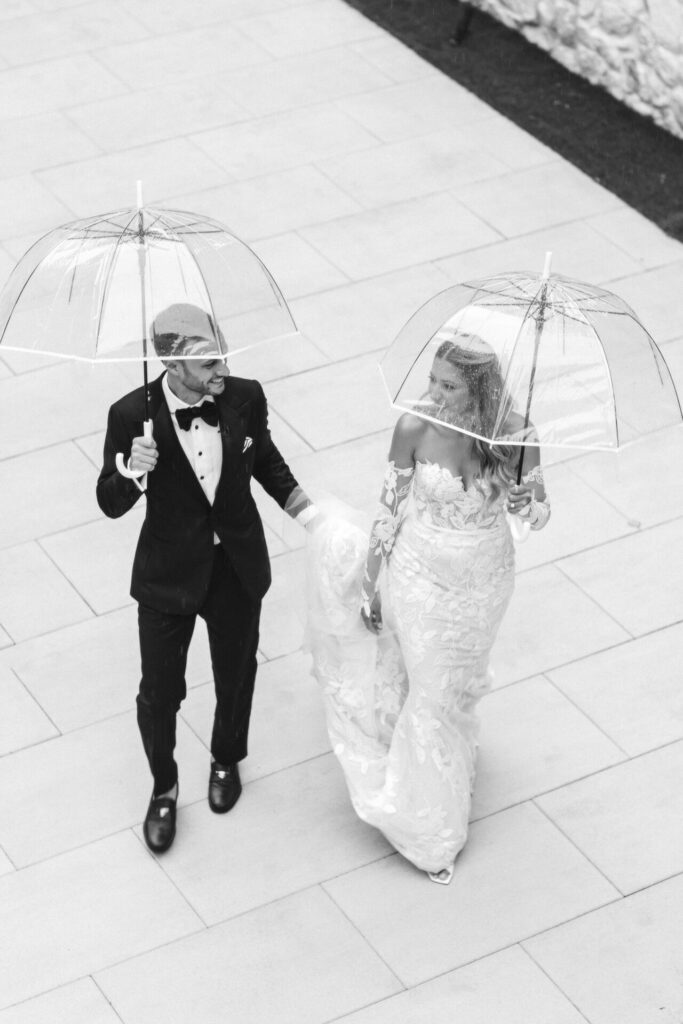 Bride and groom walk under umbrellas, viewed overhead.