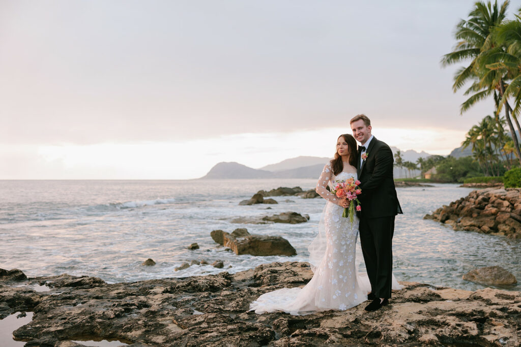Taylor and her groom pose oceanfront at sunset with mountains behind — Kapolei wedding