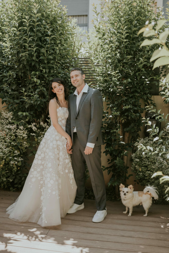 Katya Ruiz and groom hold hands outdoors with dog.