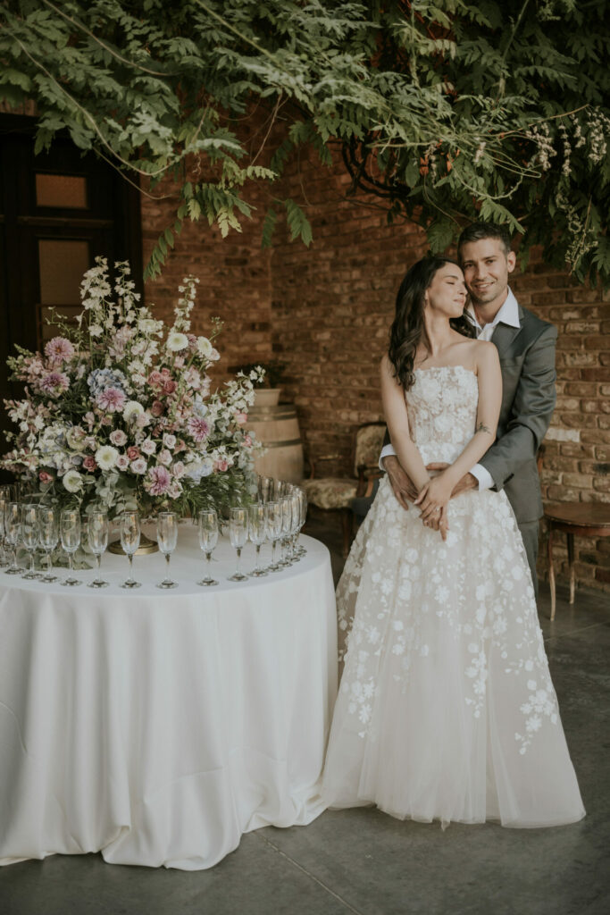 Bride and groom pose by floral table, elegant setting.