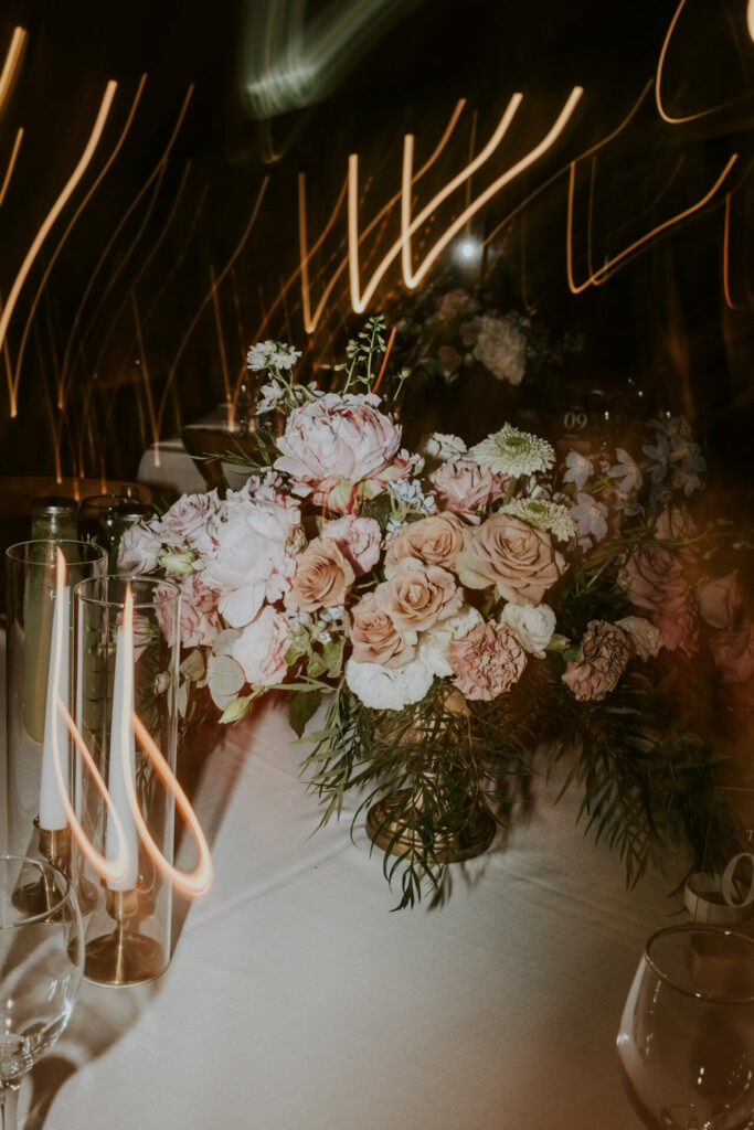 Elegant pink-white rose centerpiece, glassware, candles, light trails.