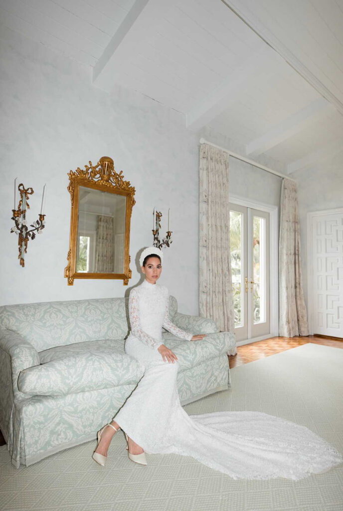 Woman in white wedding dress on green sofa, elegant room.