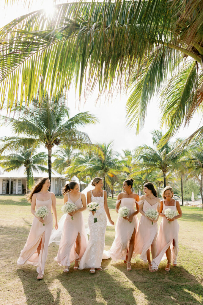 Bride and bridesmaids with bouquets under sunny palm trees.