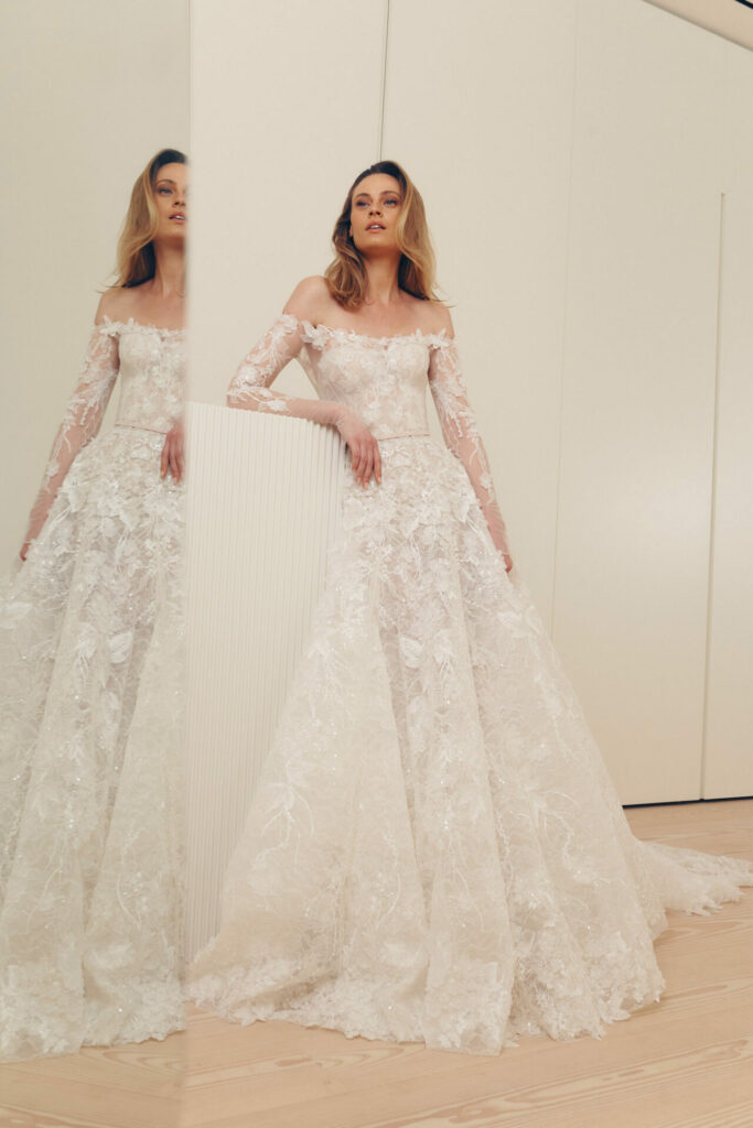 Bride in lace gown poses by mirror in modern room.