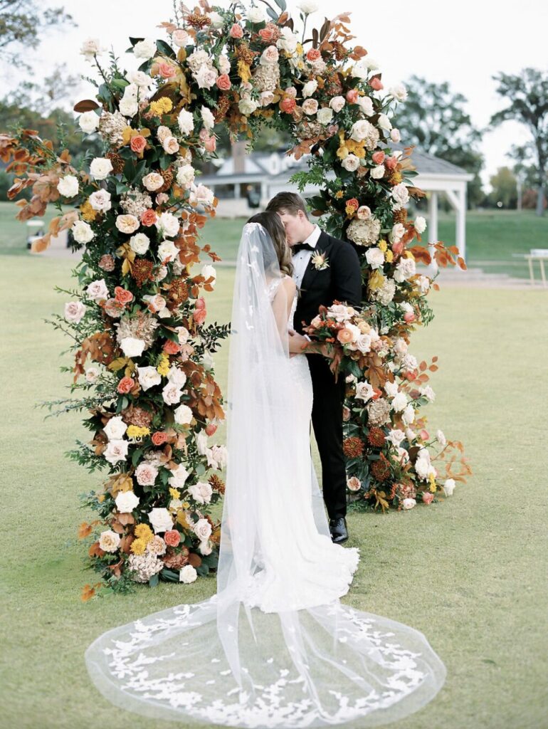 Bride and groom under floral arch in romantic setting.