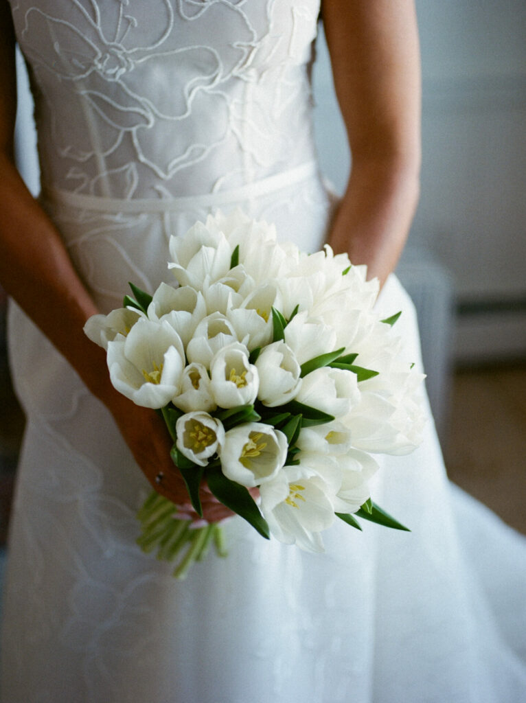 Bride in SS2026 dress holding white tulip bouquet indoors.