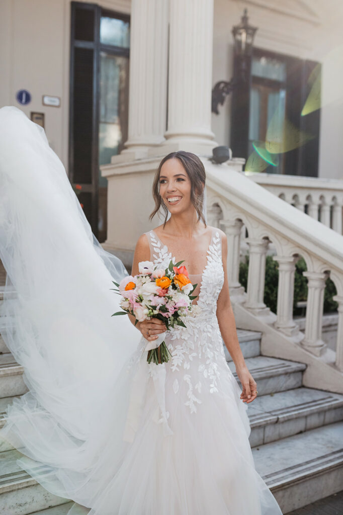 Bride in floral lace gown, holding bouquet, veil flowing.
