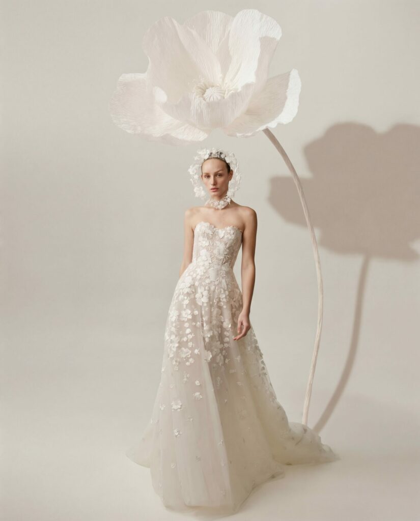 Woman in floral gown and headpiece beneath sculpted flower.