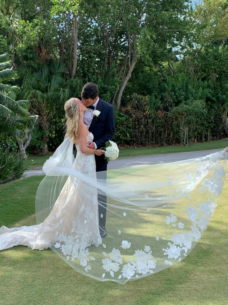Couple kisses on lawn; bride in lacy dress, veil.