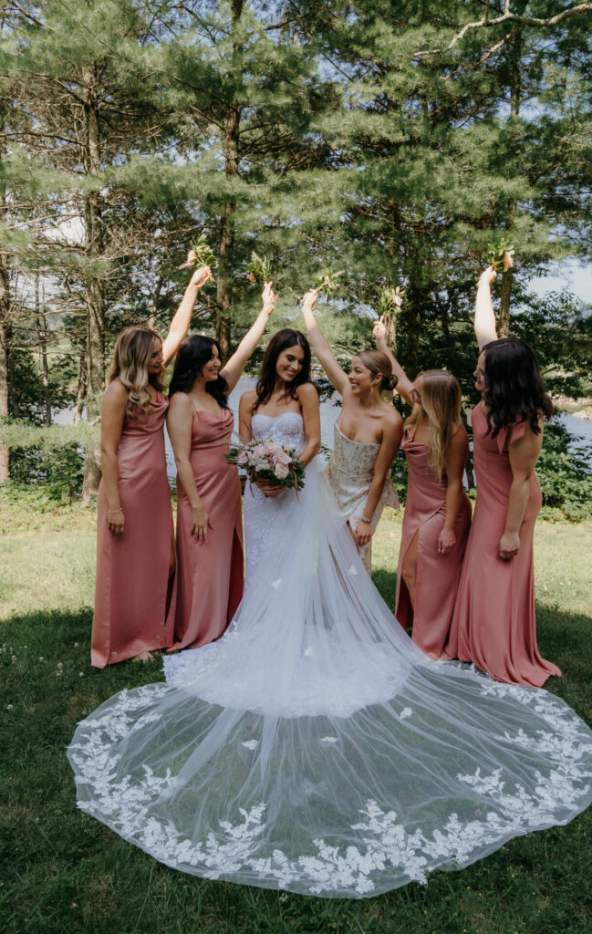 Bride and bridesmaids in pink dresses smiling outdoors.