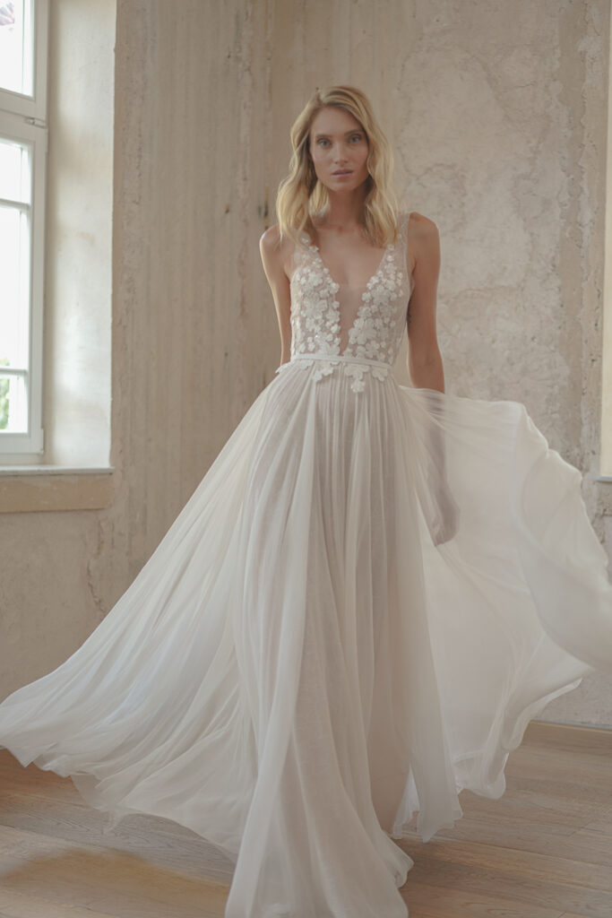 Woman in white floral gown by sunlit window.