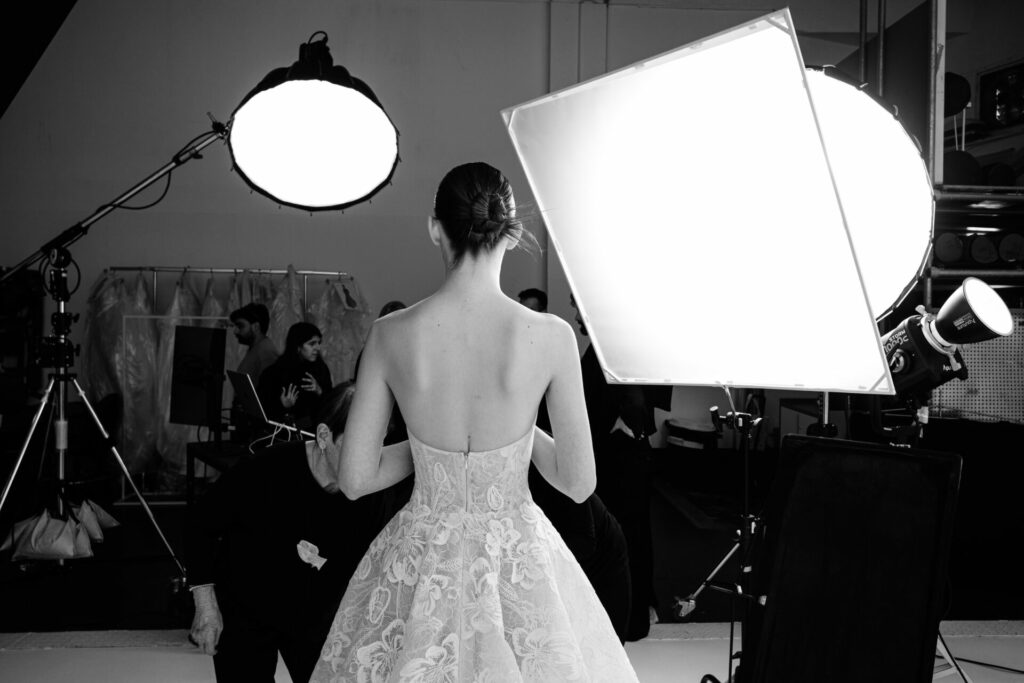 Woman in lace dress faces away amid studio bustle.